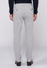 Světlé šedé kalhoty z bavlny se slim fit střihem. Mají dvě zadní kapsy s černými knoflíky a hladký povrch.