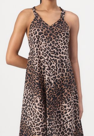 Femme portant une robe sans manches à col en V avec un motif léopard marron et noir, posant avec un bras dans le dos.
