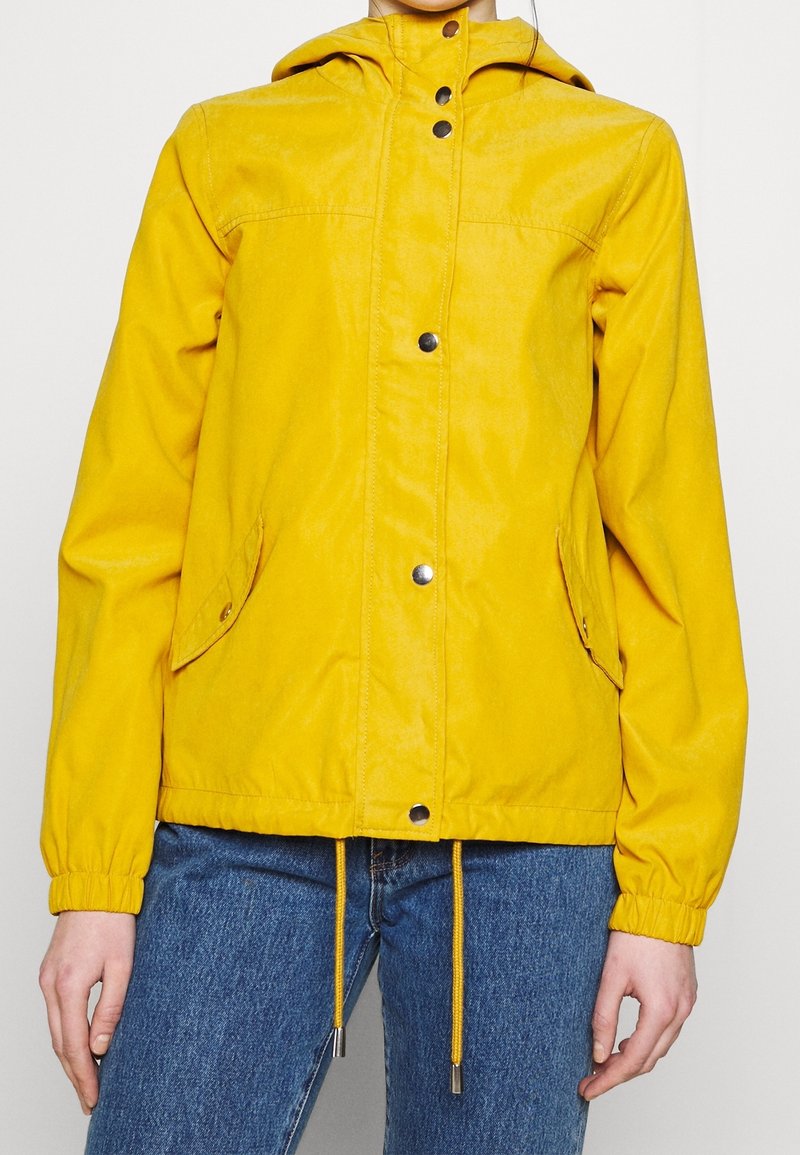 Žlutá kapucňová bunda se zapínáním na druky, elastickými manžetami, dvěma bočními kapsami a nastavitelným stahováním na dolním lemu. Hladká textilie.