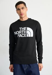 Sudadera negra de algodón con cuello redondo. Presenta un gran logotipo blanco y elementos de diseño curvados en la parte frontal. Mangas largas.