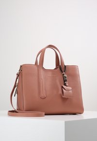 Keskikokoinen pölypinkki nahkakäsilaukku, jossa on kaksi yläkahvaa, irrotettava olkahihna, etupuolella solk yksityiskohta ja kultaisista vetoketjuista tehdyt korostukset.