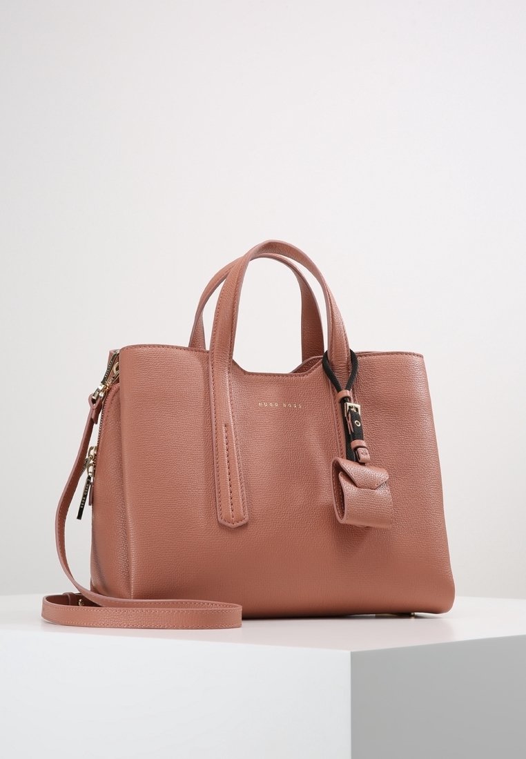 Keskikokoinen pölypinkki nahkakäsilaukku, jossa on kaksi yläkahvaa, irrotettava olkahihna, etupuolella solk yksityiskohta ja kultaisista vetoketjuista tehdyt korostukset.