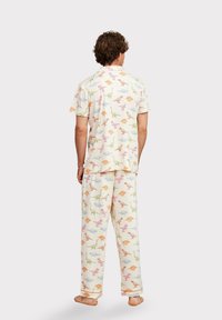 Heren pyjama-set in lichte stof met een crèmekleurige achtergrond en kleurrijke dinosaurusprints. Kort mouwtop en lange broek met elastische tailleband.