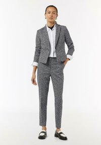 Tailored suit in a gray and white flecked pattern, featuring a fitted blazer and tapered pants, paired with a white button-up shirt and black shoes.