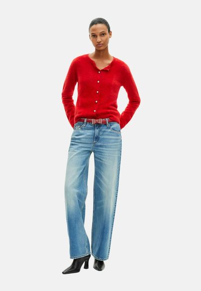 Rød cardigan med knaplukning, kombineret med falmede blå vidde-ben jeans. Sorte støvler med spids hæl fuldender looket.