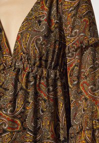 Tela marrón con un patrón de paisley en rojo, naranja y amarillo. Presenta un escote en V profundo y detalles fruncidos en la cintura y las mangas.