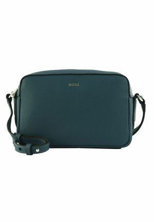Bolso de cuero en color azul verdoso, con textura suave, forma rectangular y correa ajustable. Presenta el logo de la marca en dorado en la parte frontal.