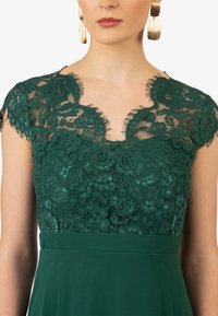 Vestito verde in pizzo con maniche corte a cappuccio, un motivo floreale e un silhouette a trapezio. Presenta un colletto scallopato e un tessuto morbido.