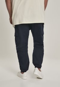 Navy cargo pants with elastic waistband and cuffs. Features multiple side pockets and a lightweight, textured fabric. Shoes are white.