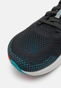 Černá sportovní bota s tkaničkami a síťovaným svrškem, zdobená akcenty v tónech modré a červeným detailem na patě. Zaoblená špička s pohodlnou podrážkou. Tkaničky v tmavě šedé barvě.