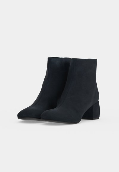 Paire de bottines en daim noir avec bouts arrondis et talons blocs, présentées sur un fond clair uni.