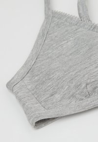 Šedý bavlněný bralet s měkkou žebrovanou texturou, nastavitelné ramínka a vlnité okraje kolem výstřihu a otvorů na paže.