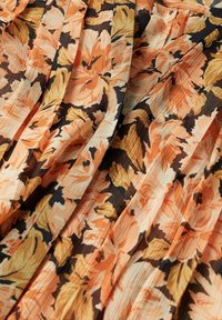 Tissu avec un motif floral pêche, jaune et noir, montrant de doux plis et une surface légèrement texturée.
