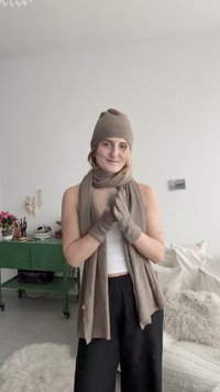 Bonnet beige en tricot, écharpe et gants. L'écharpe est drapée autour du cou, et les gants couvrent les mains. Texture de tissu doux et design décontracté.