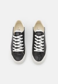 Sneakers in finta pelle di coccodrillo nera con lacci bianchi, punta tondeggiante e suola in gomma bianca. Presentano il logo "GUESS" sulla linguetta.
