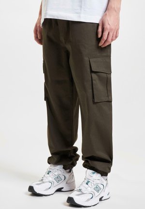 Pantalons cargo en vert olive foncé avec des poches latérales, des chevilles effilées et une coupe décontractée, assortis à des baskets de sport blanches et turquoise.