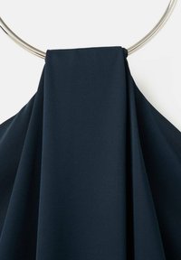 Námornícka tkanina prehodená cez strieborný kruhový prsteň, s hladkou textúrou, jemnými záhybmi a čistým, uhladeným vzhľadom.