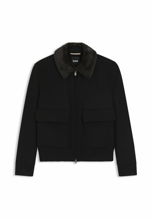 Giacca nera con zip, collo in ecopelliccia scura, due tasche frontali con pattina, polsini e girovita a coste, etichettata "BOSS" all'interno del collo.