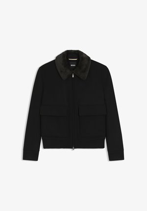 Giacca nera con zip, collo in ecopelliccia scura, due tasche frontali con pattina, polsini e girovita a coste, etichettata "BOSS" all'interno del collo.