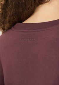 Bordeauxfarbener Sweatshirt mit geripptem Kragen, auf der Rückseite mit dem eingeprägten Text "ATHLECIA". Weicher Stoff und lässiges Design.