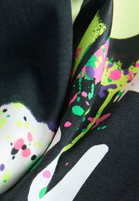 Tessuto multicolore con una combinazione di motivi di schizzi in nero, bianco e neon brillante, con superficie strutturata e finitura liscia.