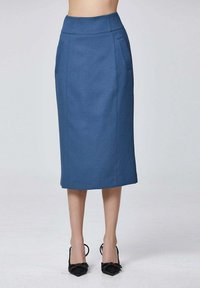 Jupe crayon taille haute bleu avec des poches latérales, portée avec des escarpins noirs à bout pointu ornés de nœuds décoratifs.