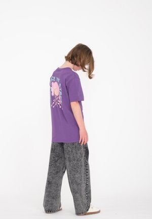 Paarse katoenen t-shirt met grafische print op de achterkant, gecombineerd met grijze wijde spijkerbroek en witte schoenen. Eenvoudig ontwerp met een losse fit.