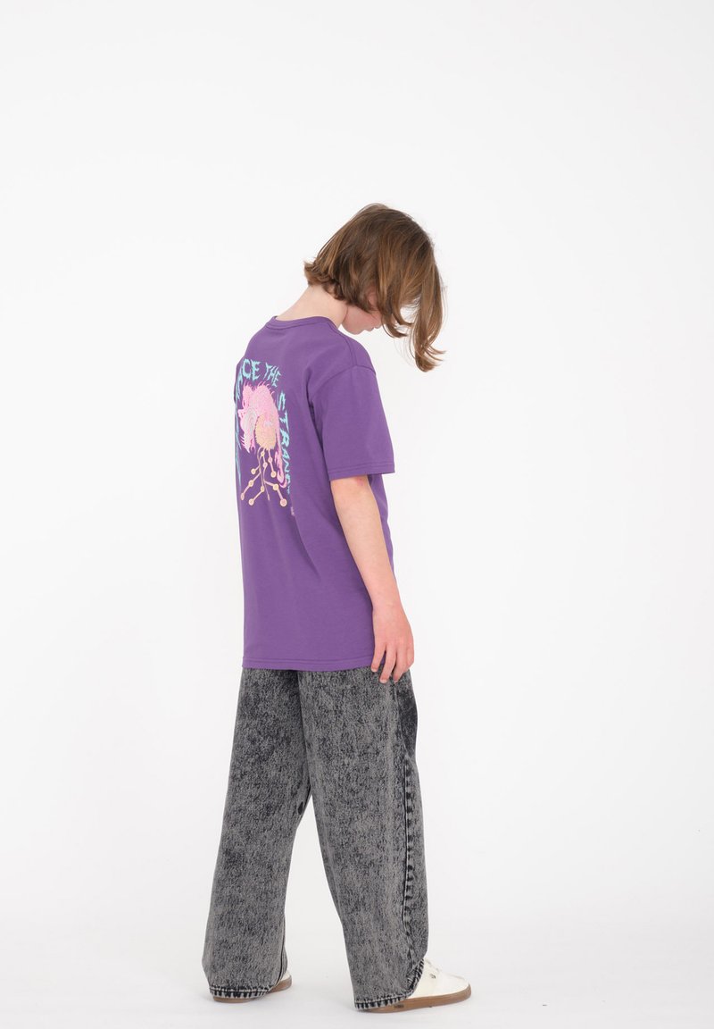 Lilla bomulds t-shirt med grafisk print på ryggen, parret med grå vidde jeans og hvide sko. Simple design med afslappet pasform.