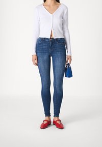 Blå skinnyjeans, vit ribbad långärmad skjorta med knappar, röda platta skor med spänne och en liten blå handväska.