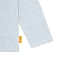 Helles blaues Langarmshirt mit einer weichen Textur und einem runden Halsausschnitt; verfügt über ein gelbes Etikett am Saum mit schwarzem Text.