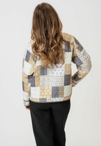 Jachet�ă din quiltat, cu patchwork, prezentând diverse modele geometric în bej, gri și alb moale. Mâneci lungi, croială lejeră, cu un hem rotund.