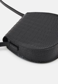 Borsa a tracolla nera realizzata in ecopelle testurizzata con motivo in coccodrillo, caratterizzata da una forma arrotondata e una tracolla slim regolabile.
