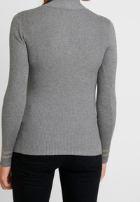 Harmaa ribbineulottu pooloneule pitkähihaisilla hihoilla, istuvalla mallilla ja hihansuiden hienovaraisilla kultaisilla raidoilla. Kankaan pinta on teksturoitu.