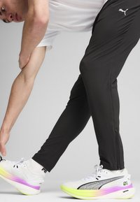 Witte sportschoenen met een gradient zool in roze en groen, gecombineerd met zwarte stretchbroek. Opvallend Puma-logo op beide.