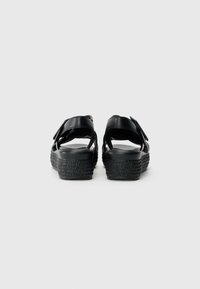 Sandales noires avec plusieurs sangles réglables, dotées d'une semelle compensée texturée et d'un matériau supérieur lisse, vues de l'arrière.