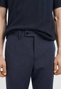 Pantalons marine avec une finition texturée, dotés d'une fermeture à bouton sur le devant, de passants de ceinture et de poches latérales, conçus pour un ajustement sur mesure.