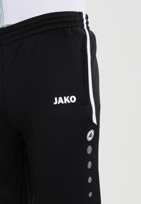 Zwarte sportbroeken met witte zijstrepen, logo en gestippelde accenten. Gemaakt van ademend materiaal met een elastische tailleband.