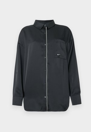 Camicia nera a maniche lunghe con bottoni, con piping bianco lungo i bottoni e una tasca sul petto che presenta un piccolo logo Nike bianco.