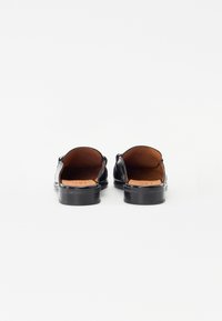 Black leather slip-on shoes featuring a low heel, rounded shape, and open back, with a smooth exterior and tan insole detail.
