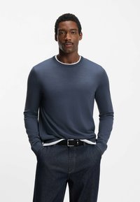 Maglione girocollo a maniche lunghe color blu navy con finitura testurizzata, caratterizzato da un dettaglio colletto bianco. Abbinato a jeans in denim scuro e cintura nera.