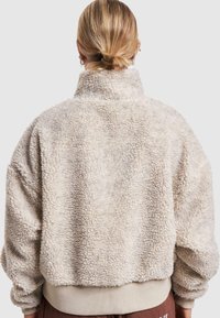 Fleece jacket in soft cream color with a high collar, oversized fit, textured surface, and ribbed hem. Features dropped shoulders and elastic cuffs.