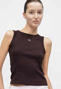 Αμάνικο, ριμπ πλεκτό τοπ σε σκούρο βουργουνδί με εφαρμοστή γραμμή. Διαθέτει μικρό μαύρο λογότυπο στην πάνω μπροστινή πλευρά. Λεία υφή.