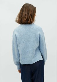 Maglione a coste di un blu chiaro, con una vestibilità comoda e un collo arrotondato. Tessuto morbido e orlo posteriore leggermente accorciato, abbinato a pantaloni blu navy.