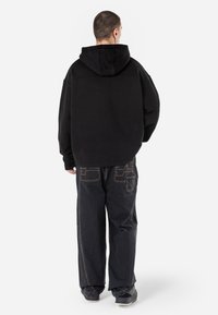 Felpa nera oversize con superficie testurizzata. Abbinata a pantaloni in denim scuro con cuciture a contrasto e design delle tasche posteriori.