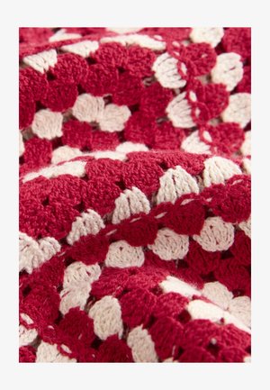 Raudonos ir kūdros spalvos nėrimo antklodė su tekstūruotu, geometriniu raštu. Minkšta siūlai su pūkuotu paviršiumi ir iškilusiais dygsniais.