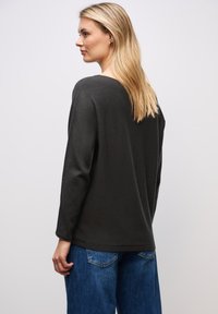 Maglione grigio scuro, morbido e oversize, con maniche lunghe e scollatura rotonda, abbinato a jeans in denim blu. Design semplice e stile casual.
