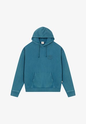 Zila kapuce ar priekšējo kangaroo kabatu un smalku apļveida logo kreisajā krūtī, novietota uz baltas virsmas.