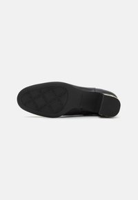 Suela de zapato de cuero negro con un patrón de textura en la banda de rodadura, con un tacón ligeramente elevado y bordes suaves. Estructura de goma duradera visible.