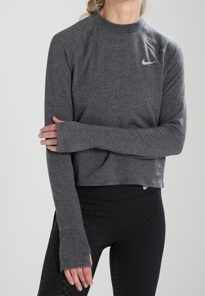 Top sportivo grigio a maniche lunghe con collo alto e polsini con foro per il pollice, dotato di un piccolo logo Nike bianco sul petto sinistro, abbinato a leggings neri.