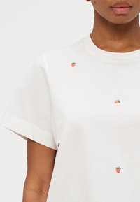 T-shirt in cotone bianco con piccoli disegni di fragola ricamati in rosso e verde, colletto tondo e maniche corte.